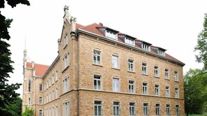 Un edificio de varios pisos con una fachada simétrica, ventanas grandes y un tejado de tejas rojas.