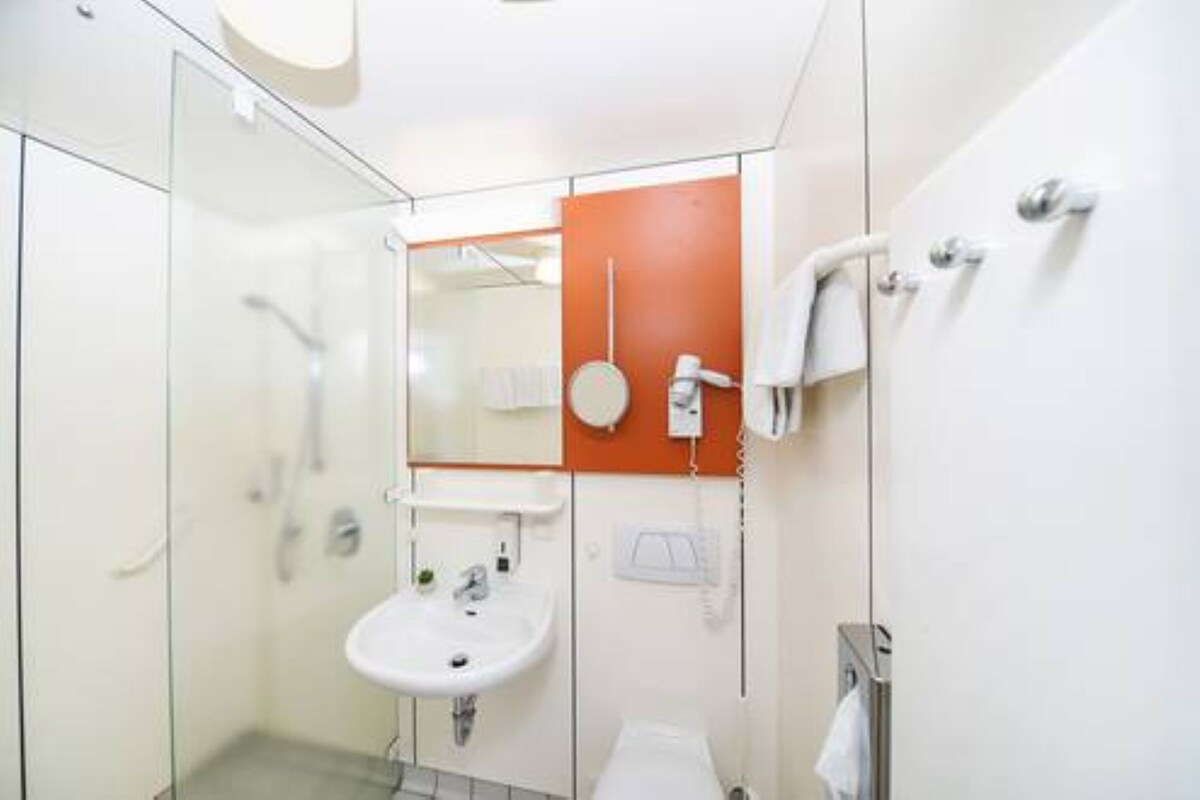 Un baño moderno con cabina de ducha de vidrio, un lavabo blanco y un espejo con una pared de acento naranja.