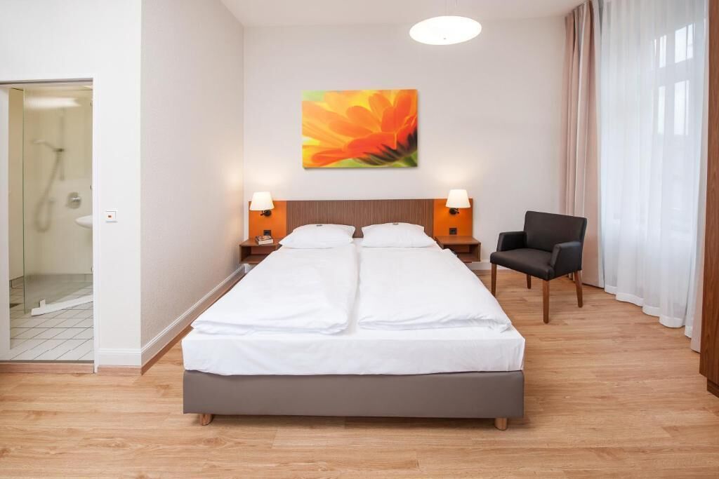 A hotel room with a double bed, two bedside lamps, a chair, and a large window with curtains.