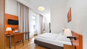 Una habitación de hotel con cama, escritorio, televisión y un cuadro en la pared.