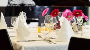 Una mesa de comedor dispuesta con servilletas blancas, copas de vino y un piano al fondo.