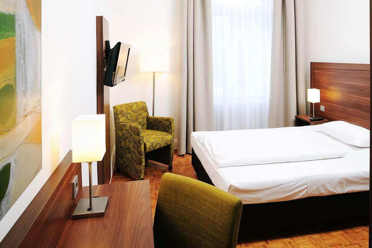 Habitación de hotel con cama, escritorio con lámpara, silla y un cuadro en la pared.
