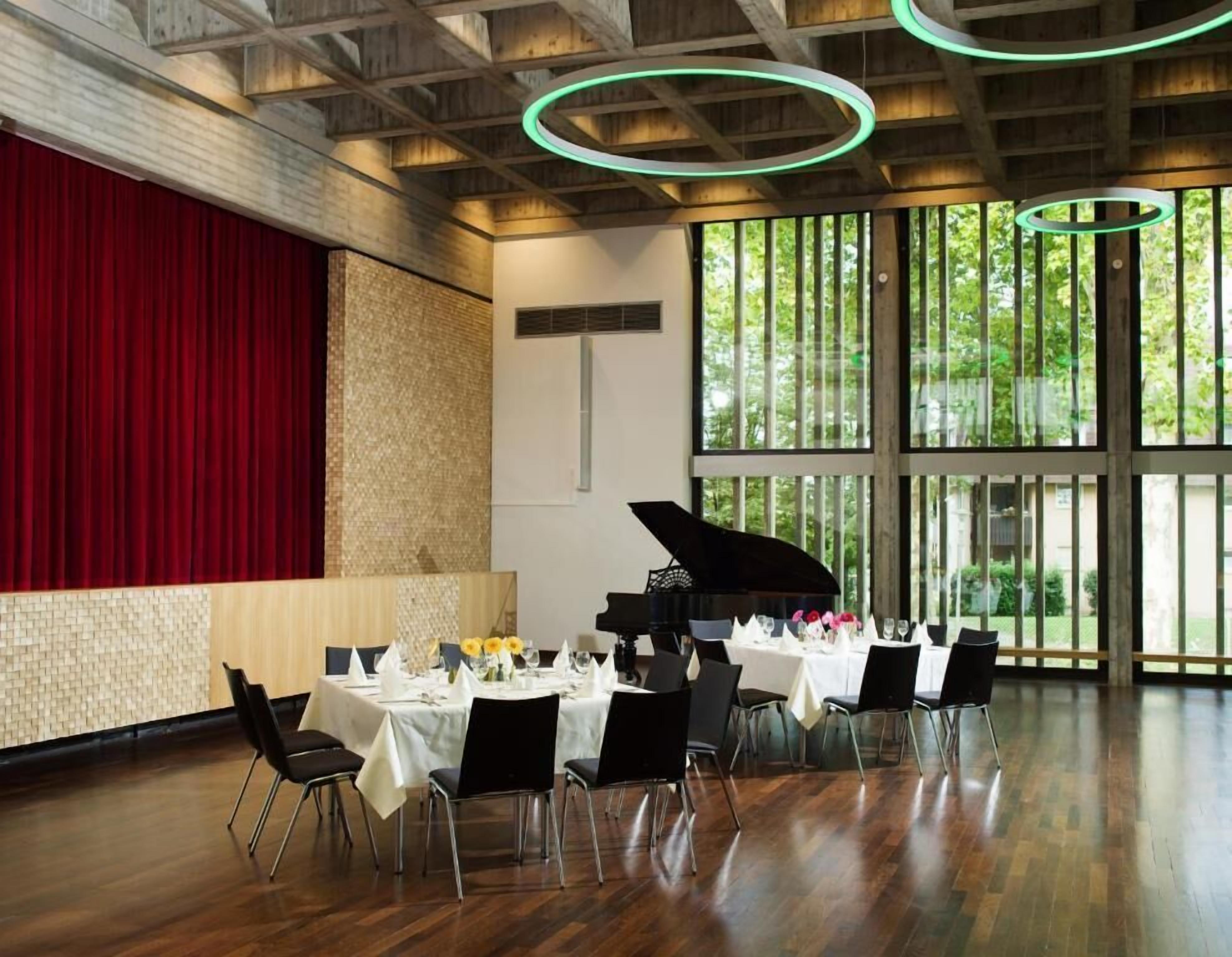 A spacious room with a grand piano, large windows, and a red curtain backdrop.
