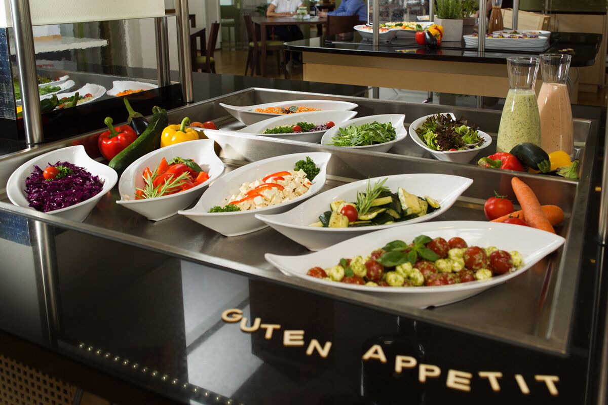 Een buffet met diverse gerechten, waaronder salades, groenten, en een sectie met de tekst 'GUTEN APPETIT'.