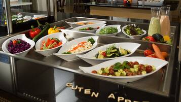 Een buffet met diverse gerechten, waaronder salades, groenten, en een sectie met de tekst 'GUTEN APPETIT'.