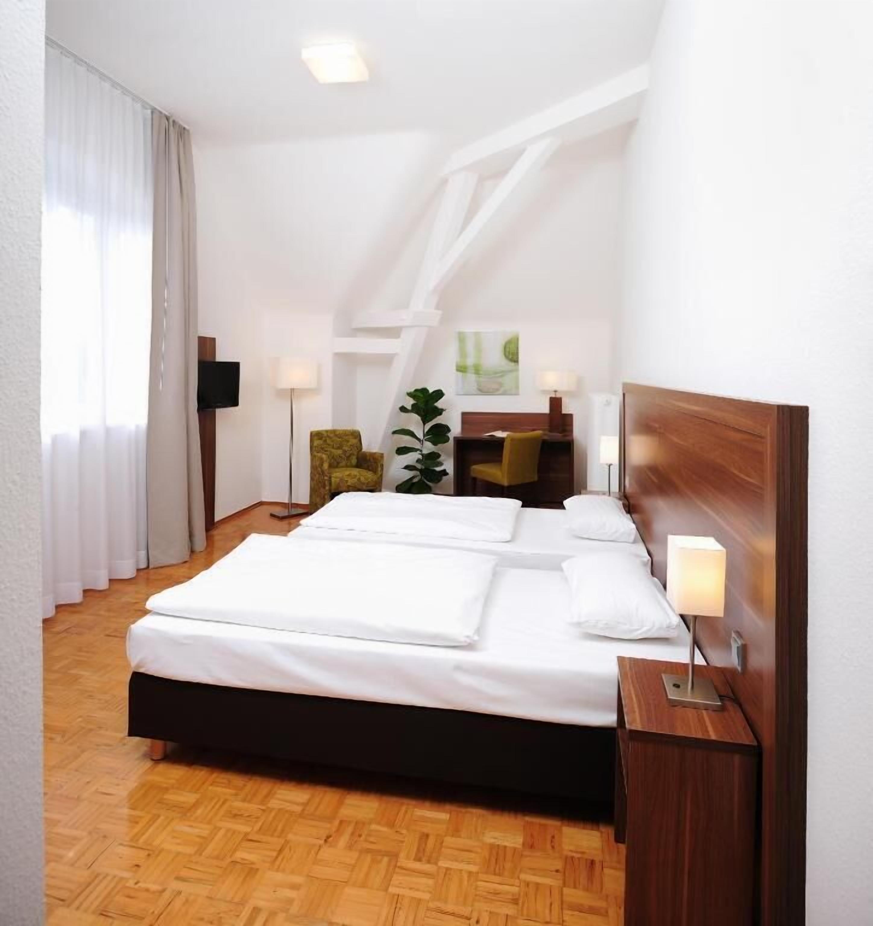 A hotel room with a large bed, a desk, a chair, a plant, and a TV.