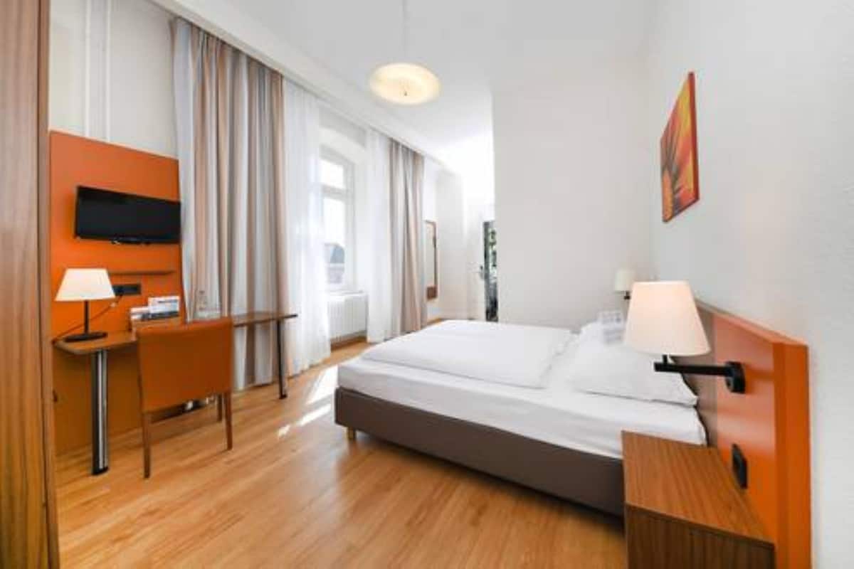 Habitación de hotel con cama, escritorio, silla, televisor y un cuadro en la pared.