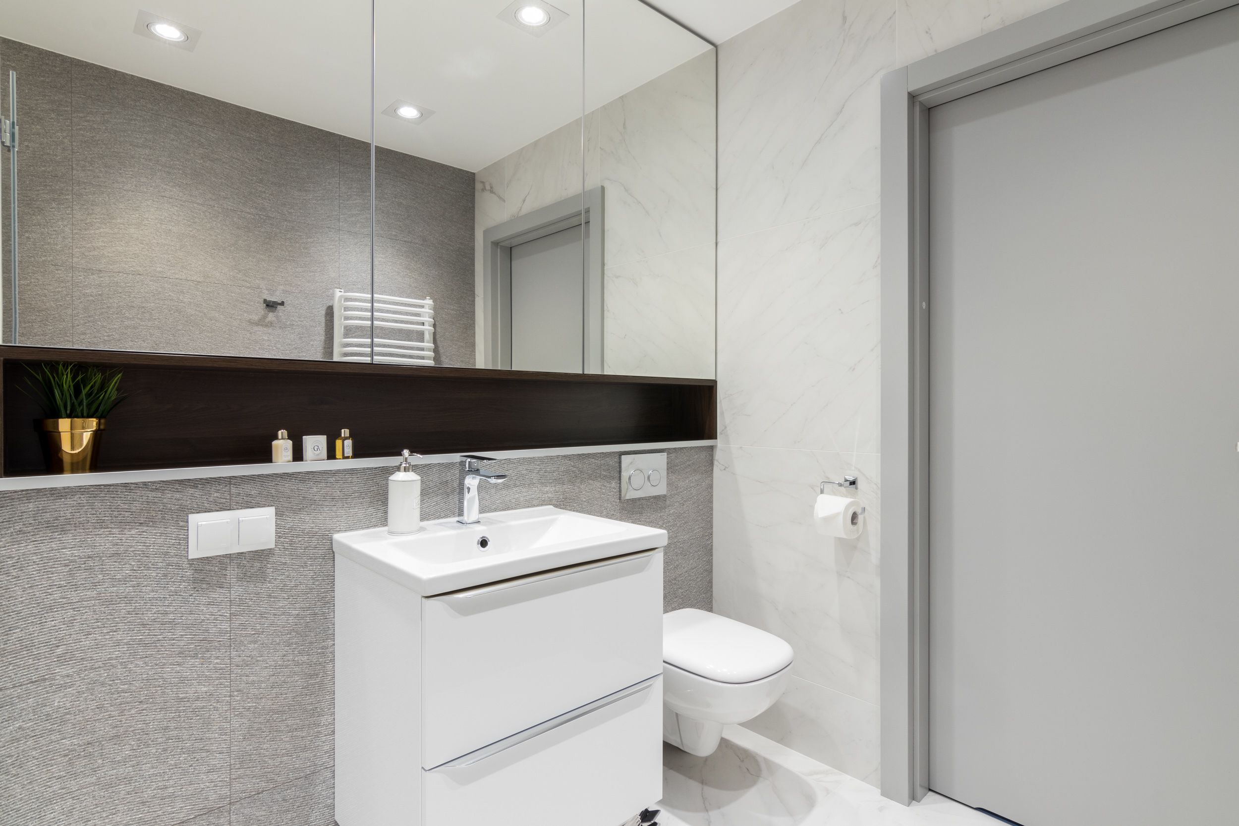 Une salle de bain moderne avec un lavabo blanc, un miroir au-dessus et des toilettes.