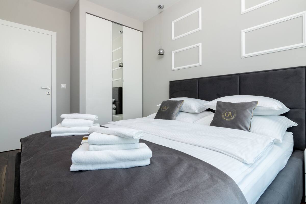 A modern hotel room with a neatly made bed, a large mirror, and a door with a handle.