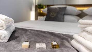 Un lit bien fait, avec du linge de lit blanc, une couverture grise et deux articles de toilette portant la lettre « G » sur une surface grise.