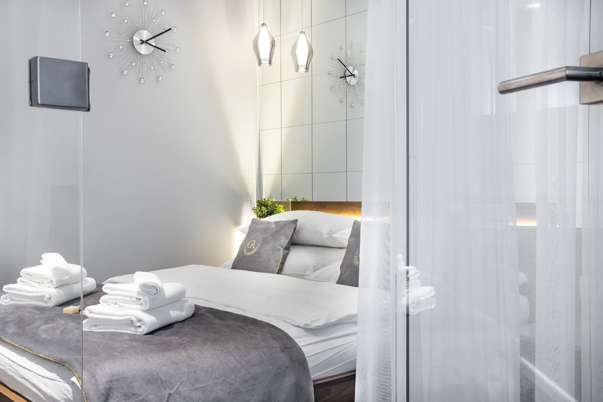 A modern hotel room with a neatly made bed, a large mirror, and a wall clock.