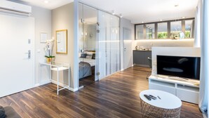 A modern living room with a flat-screen TV, a small round table, and a glass partition separating the living area from a bedroom. - GA Luxury Apartments Wawrzynca 21 (Kraków)