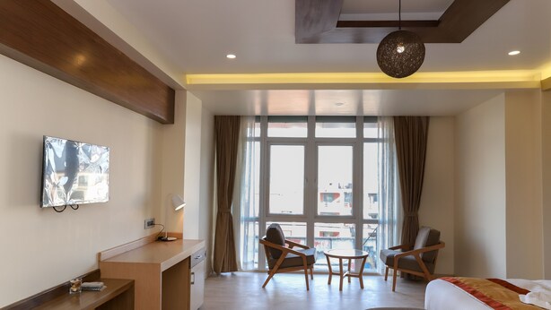 A modern hotel room with a bed, desk, two chairs, a small table, and a large window with curtains. - Retro Hotel and Spa (Kathmandu)