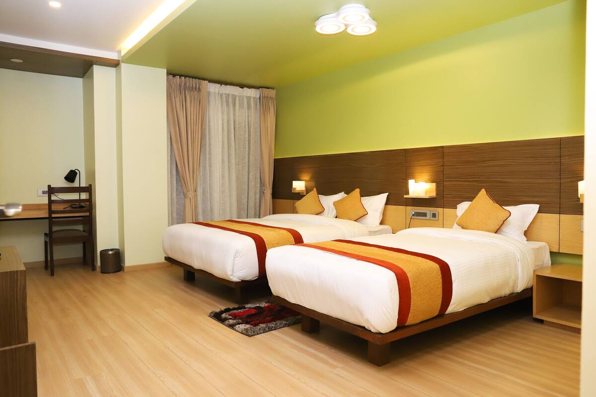 A hotel room with two beds, wooden headboards, a desk, and a trash bin.