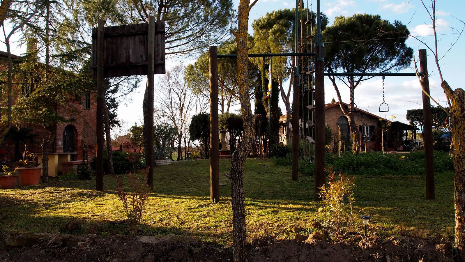 A playground with swings and climbing structures, surrounded by trees and a brick building.