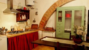 A kitchen with a gas stove, red curtains, a wooden table, and a green cabinet. - Agriturismo La Terra (Montepulciano)