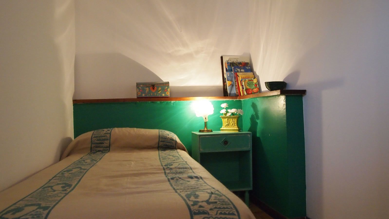 Une petite pièce agréable, dotée d’un lit, d’une table de chevet et d’une étagère fixée au mur.