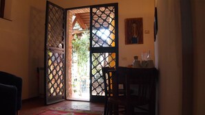 A room with a wooden door leading to an outdoor area, a table with a chair, and a painting on the wall. - Agriturismo La Terra (Montepulciano)