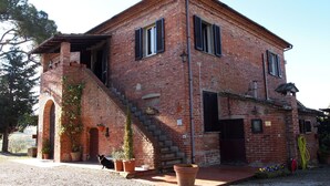 A two-story brick building with a staircase leading to the upper floor, potted plants, and a dog in front. - Agriturismo La Terra (Montepulciano)