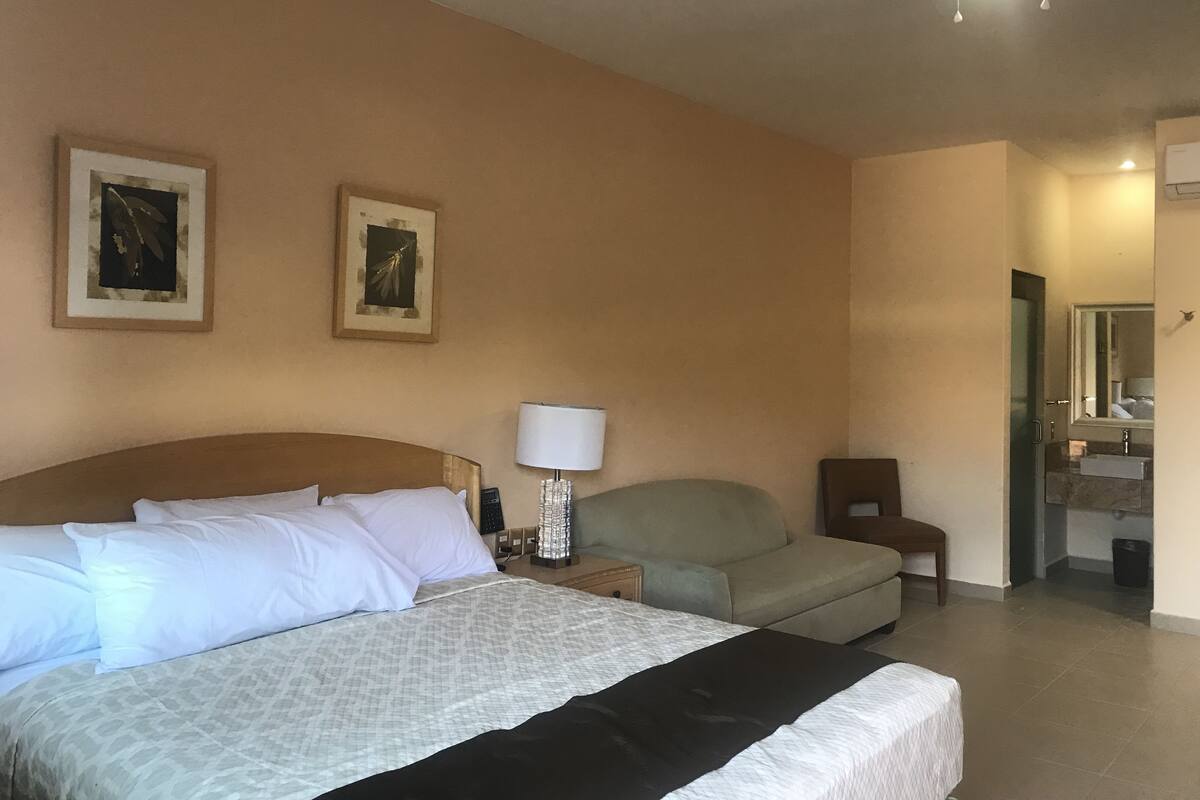 Ein Hotelzimmer mit Bett, Nachttisch, Lampe, Stuhl und einer Tür zu einem Badezimmer.
