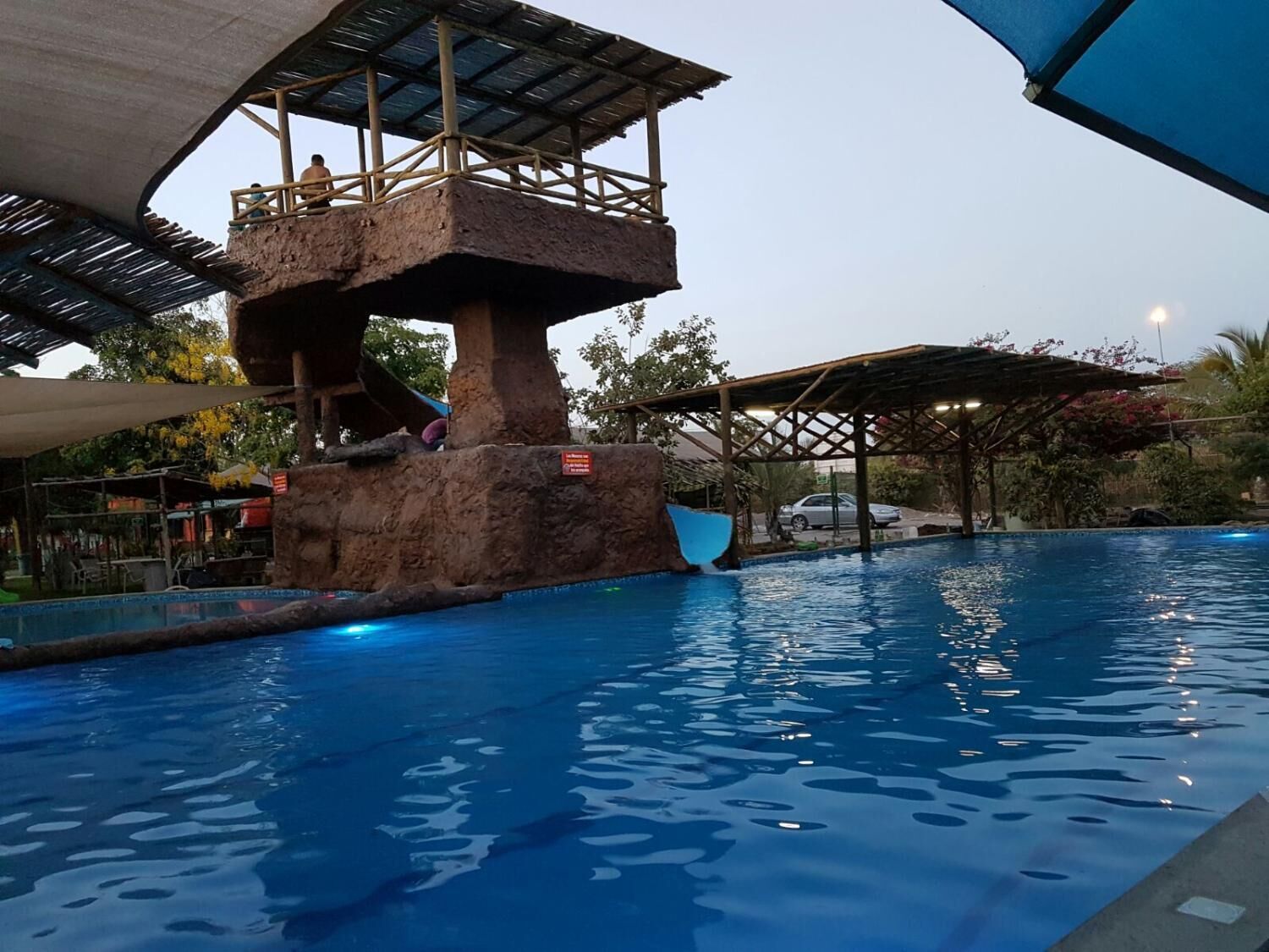 Una piscina con una estructura rocosa y un área de descanso cubierta.
