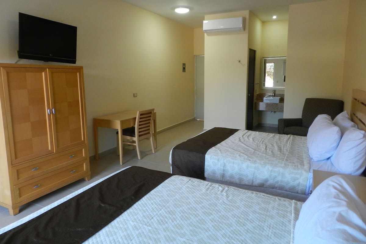Ein Hotelzimmer mit zwei Betten, einem Schreibtisch, einem Stuhl, einem Fernseher und einer Klimaanlage.