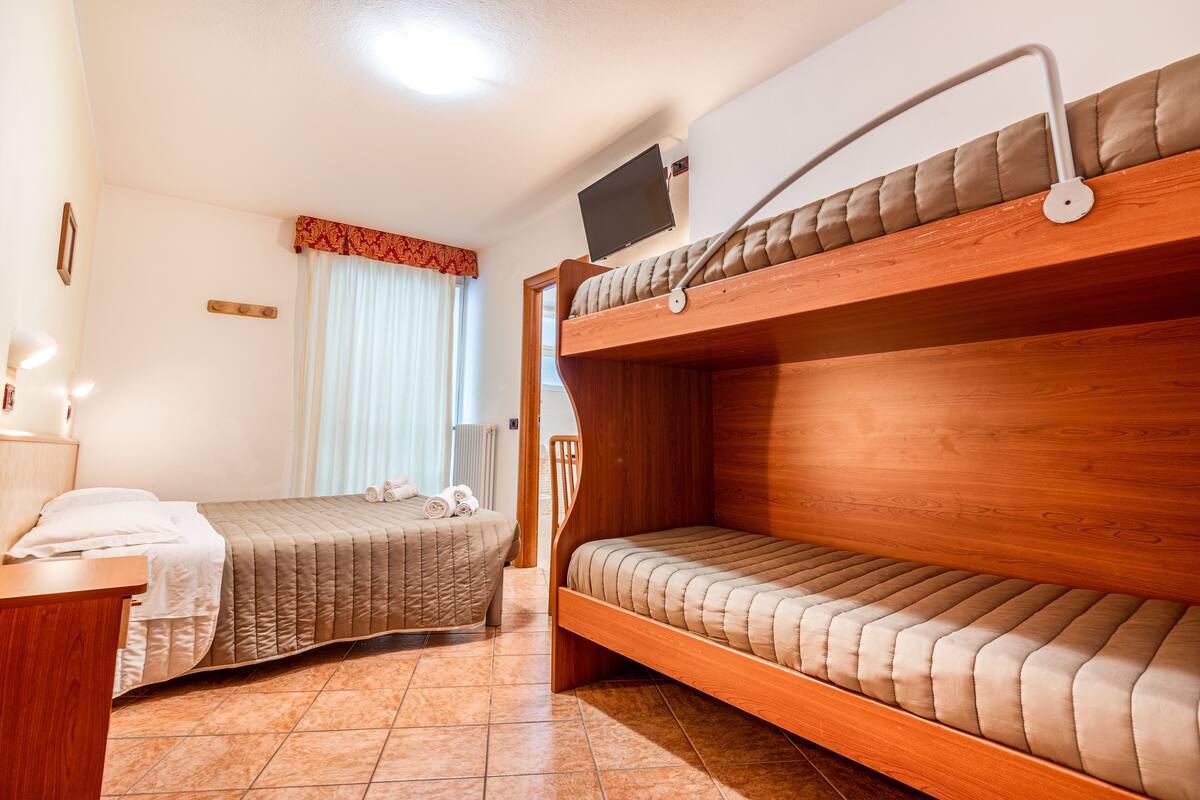 A room with two bunk beds, a desk with a lamp, and a television mounted on the wall.