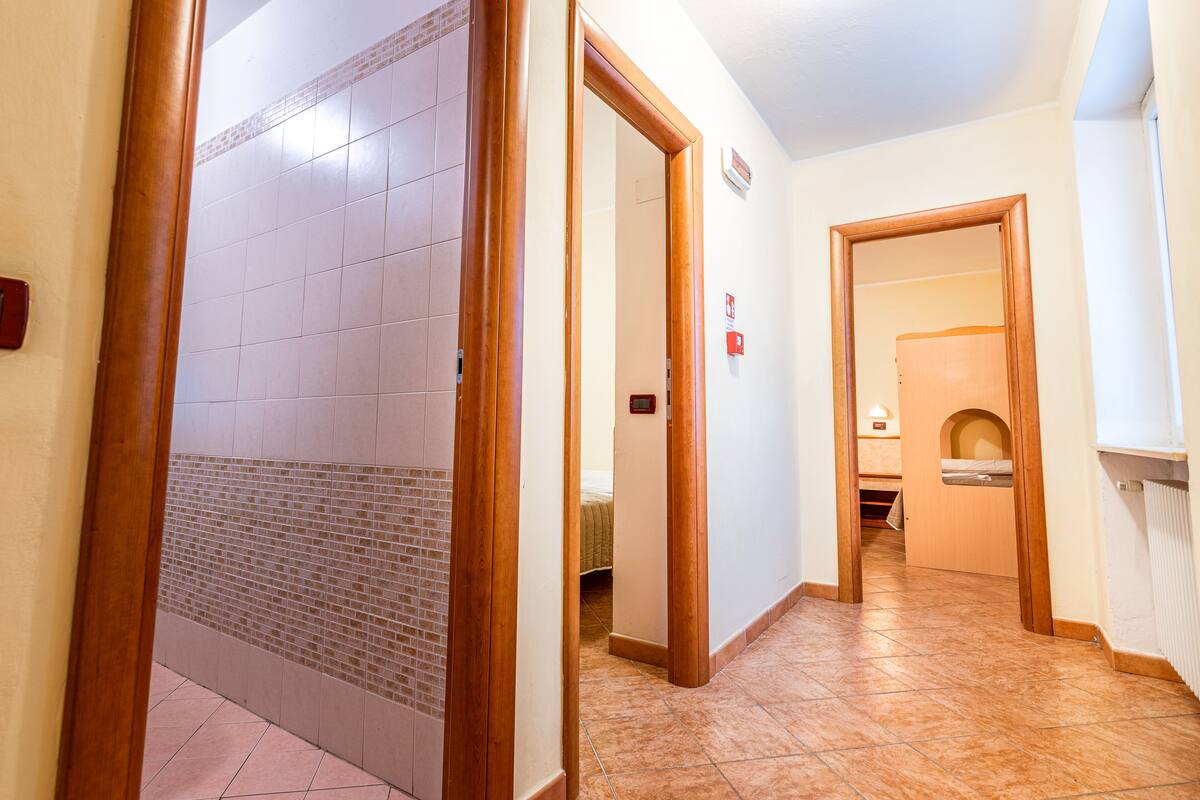 A hallway with a tiled floor, wooden doors, and a visible bed in the background.