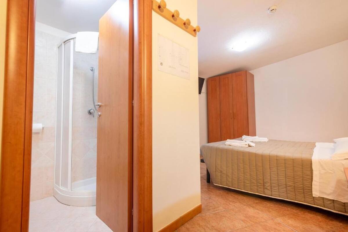 A bedroom with a bed, a wooden wardrobe, and a shower area.