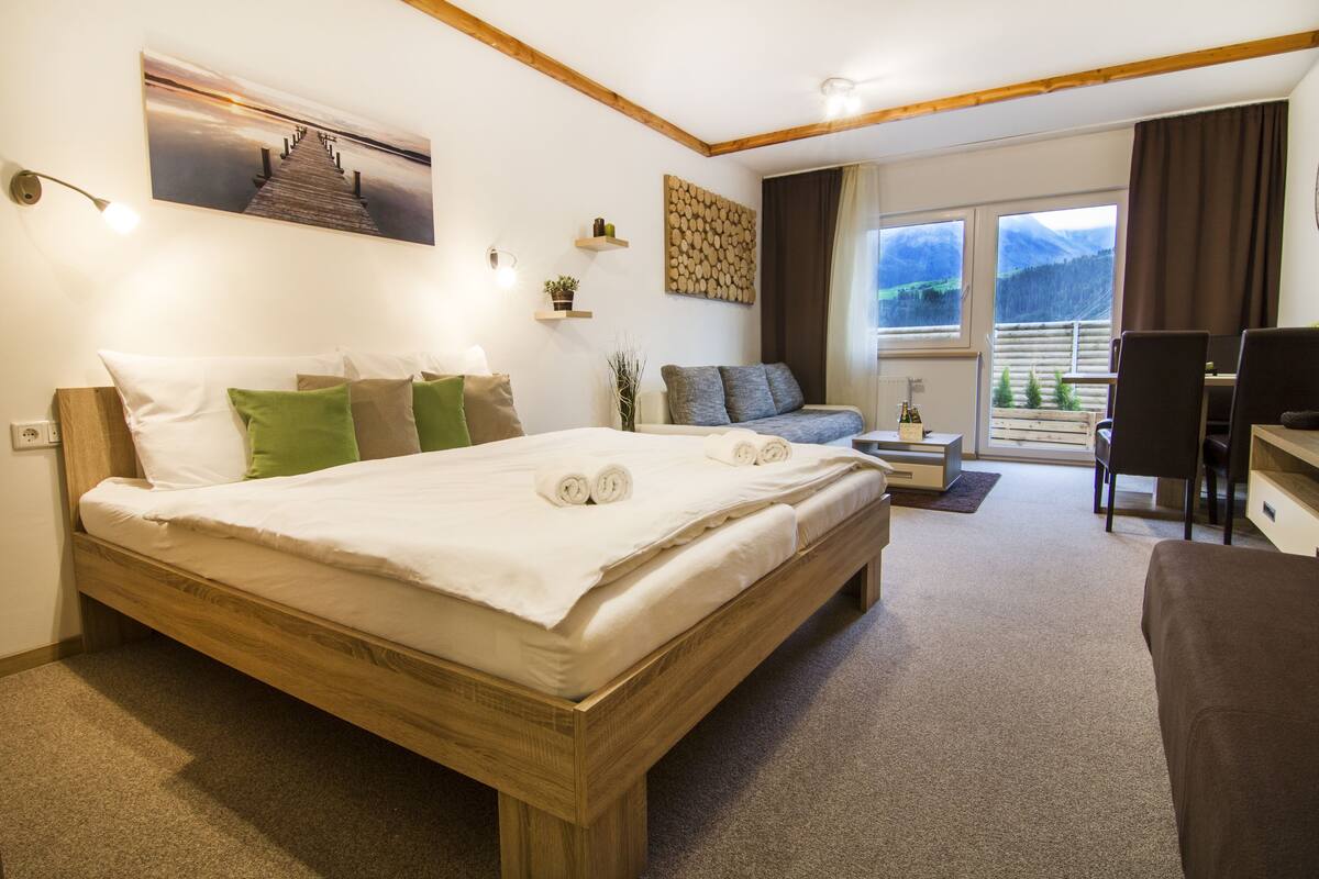 A hotel room with a large bed, a sofa, a desk, and a view of mountains through the window.