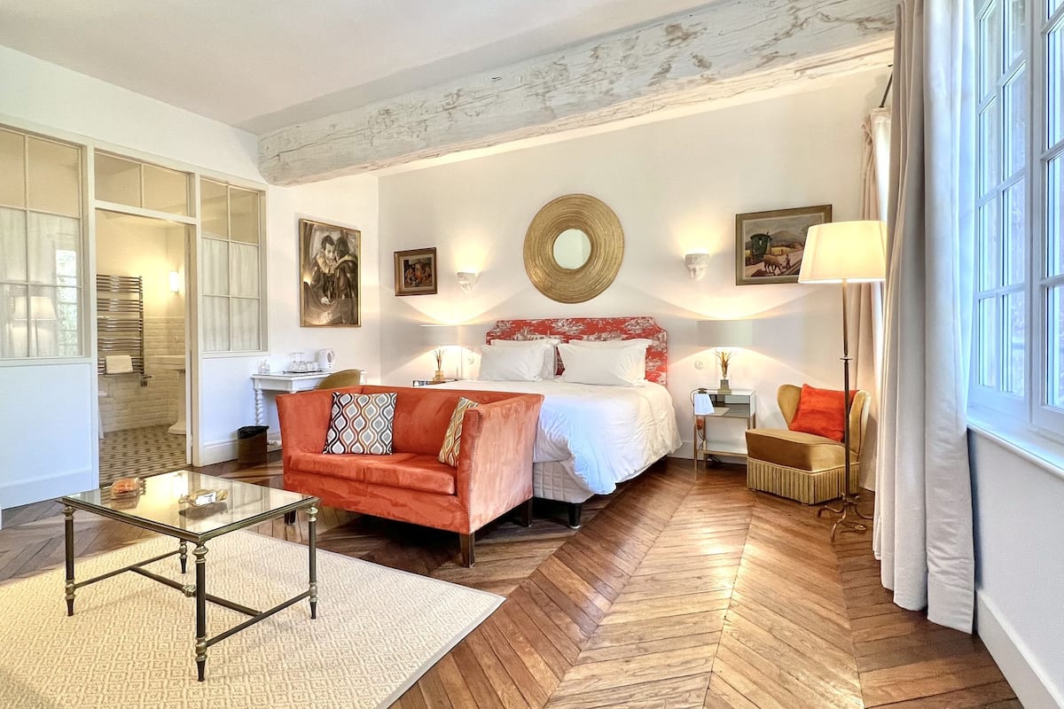 A hotel room with a bed, a sofa, a glass coffee table, a desk, and a chair.