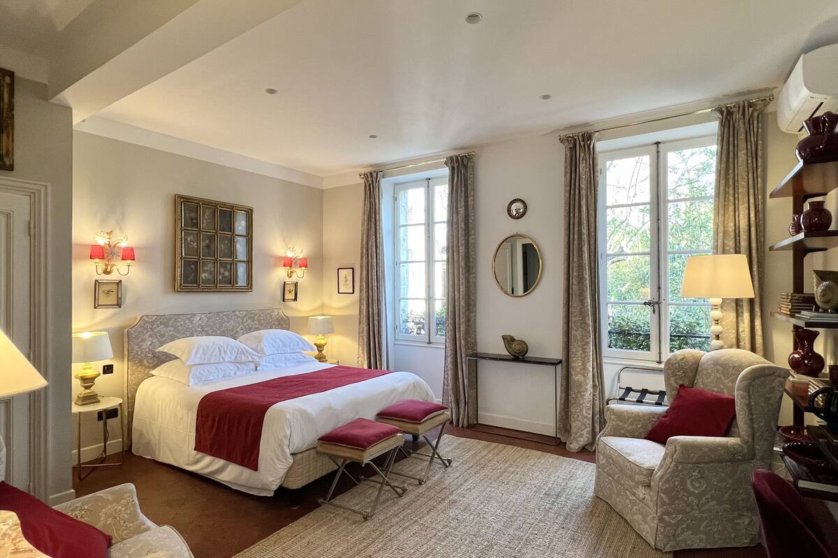 A well-lit bedroom with a large bed, bedside tables with lamps, a mirror, and a window with curtains.