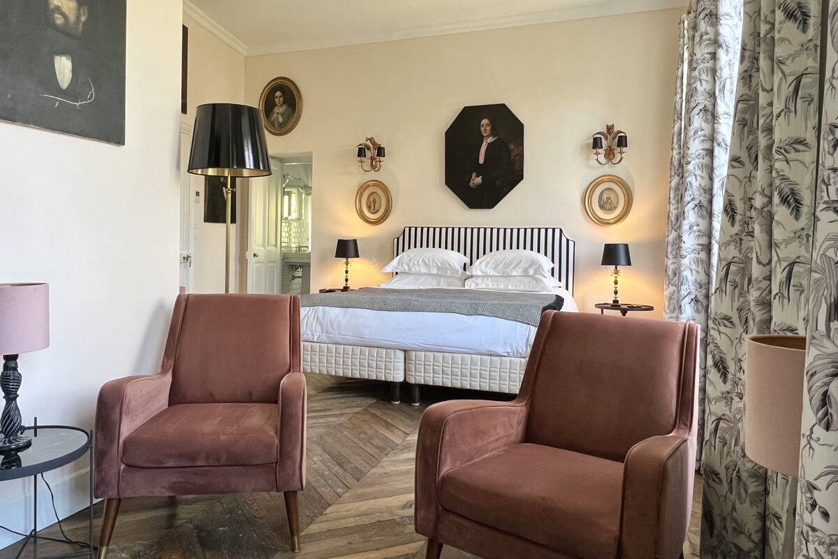 A bedroom with a large bed, two chairs, a desk, and a mirror.