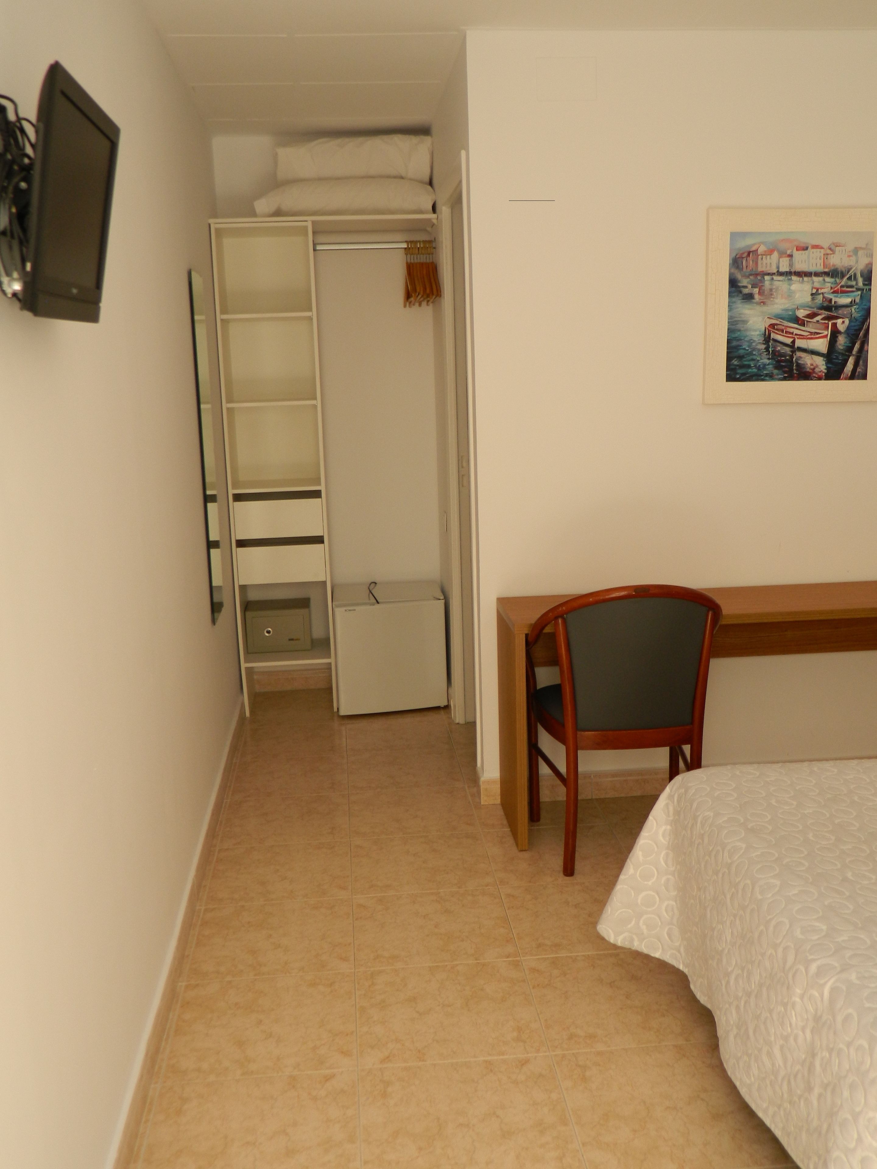 A bedroom with a bed, a desk, a chair, a wardrobe, and a television.