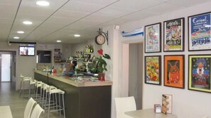 Un interior de restaurante con una zona de bar, sillas blancas y varios carteles en las paredes.