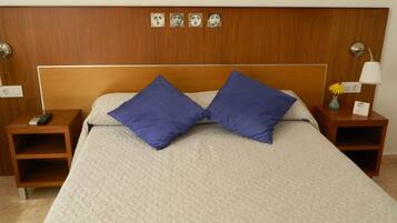 Habitación de hotel con cabecera de madera, dos mesitas de noche, cama con colcha estampada y dos almohadas azules.