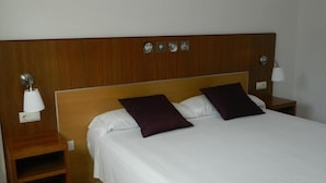 Una habitación de hotel con cabecera de madera, dos almohadas, una colcha blanca y dos mesitas de noche con lámparas.