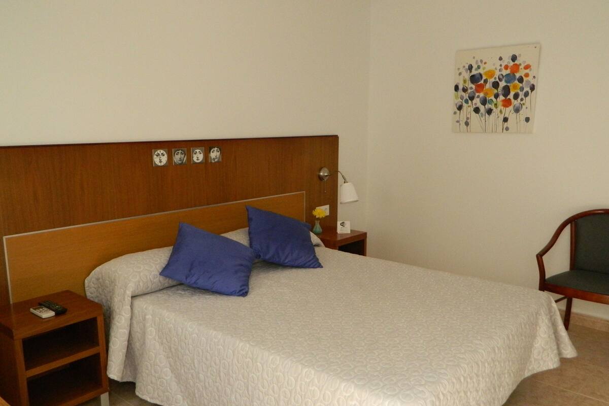 A neatly made bed with a wooden headboard, two pillows, a bedside table with a lamp, and a chair.