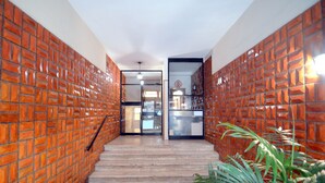 A hallway with brick-patterned walls, a staircase leading to a room, and a plant in the foreground.