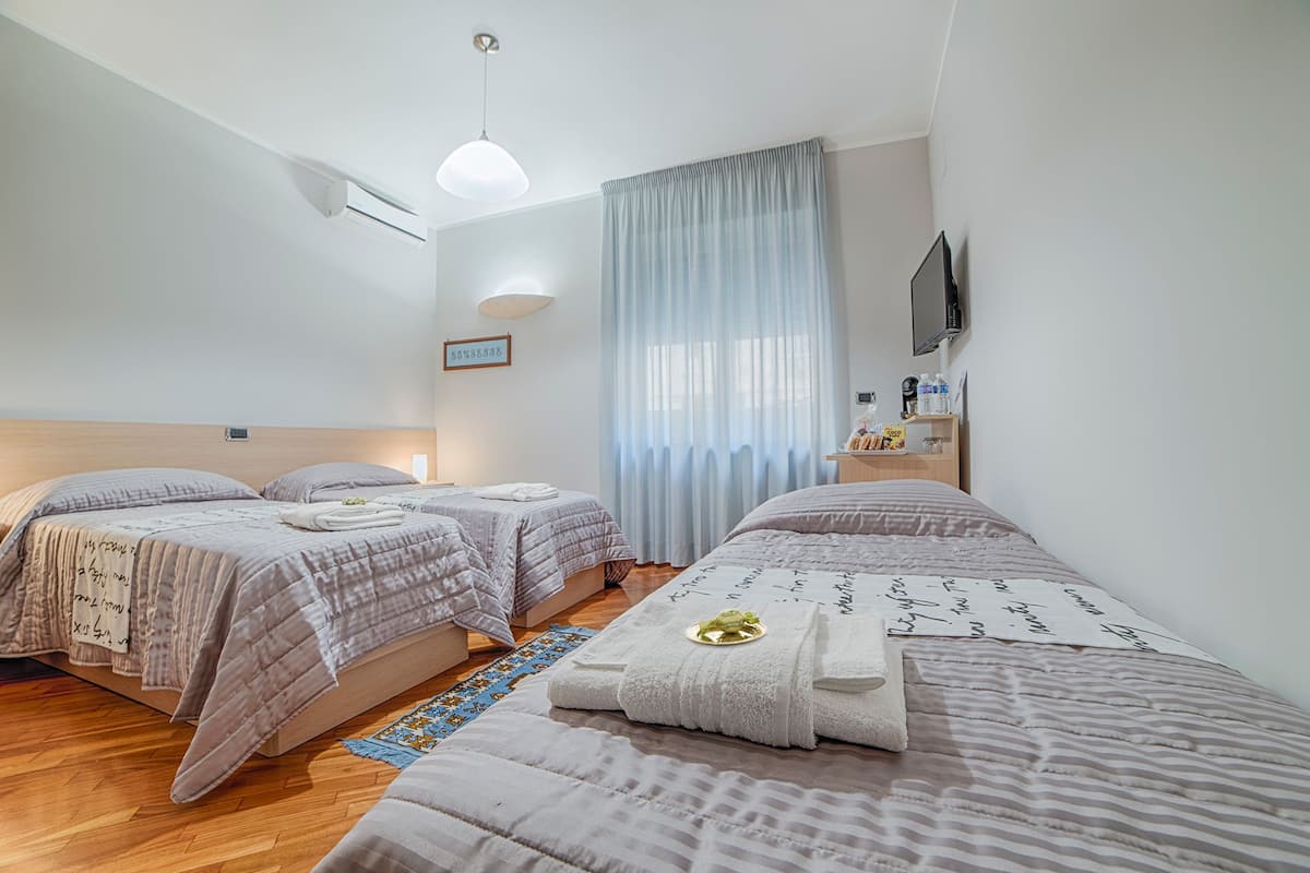 A hotel room with two beds, a flat-screen TV, a small table with toiletries, and a window with sheer curtains.