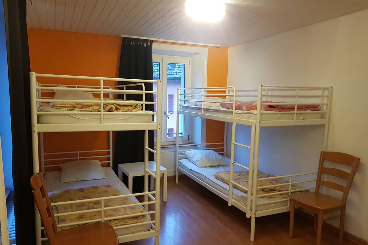 A dormitory room with bunk beds, a small table, and a chair.