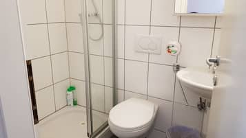 Un baño con ducha de vidrio, inodoro, lavamanos y un cubo de basura.