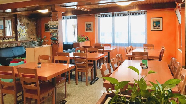 A restaurant with wooden tables and chairs, a counter with a menu, and a wall with framed pictures. - Bellpark Hostel (Kriens)
