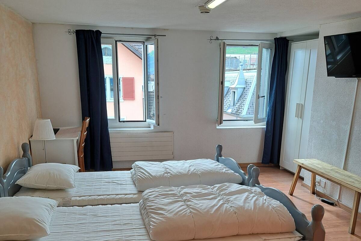 A room with two beds, a desk, a chair, a TV, and windows with curtains.
