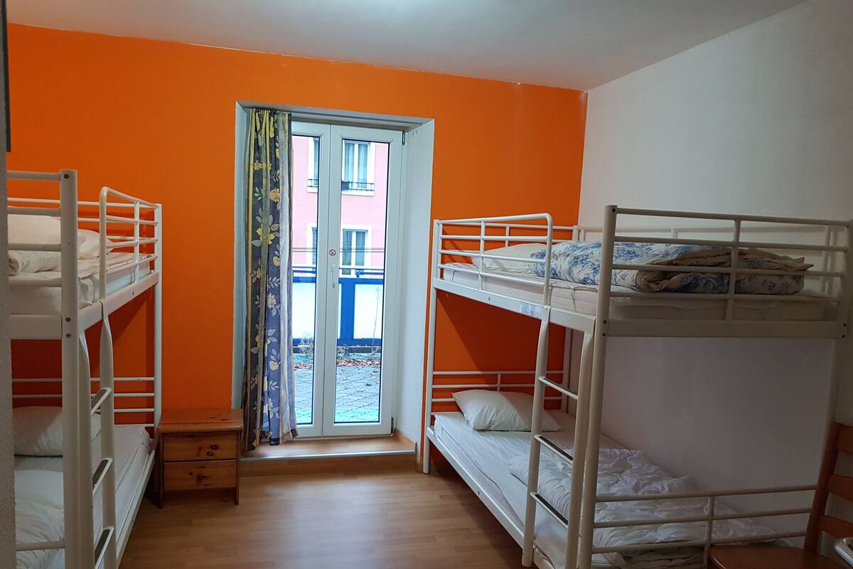A dormitory room with bunk beds, a wooden floor, and a door leading to an outdoor area.