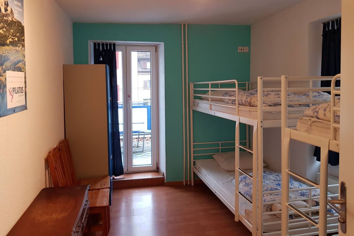 A room with bunk beds, a wooden bench, a door with curtains, and a poster on the wall.