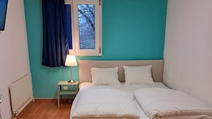 A bedroom with a bed, a nightstand, a window with curtains, and a radiator. - Bellpark Hostel (Kriens)