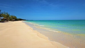 Una playa con agua turquesa cristalina, una orilla arenosa y algo de vegetación a la izquierda.