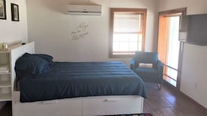 Un dormitorio con cama, una silla, un televisor y una ventana con persianas.
