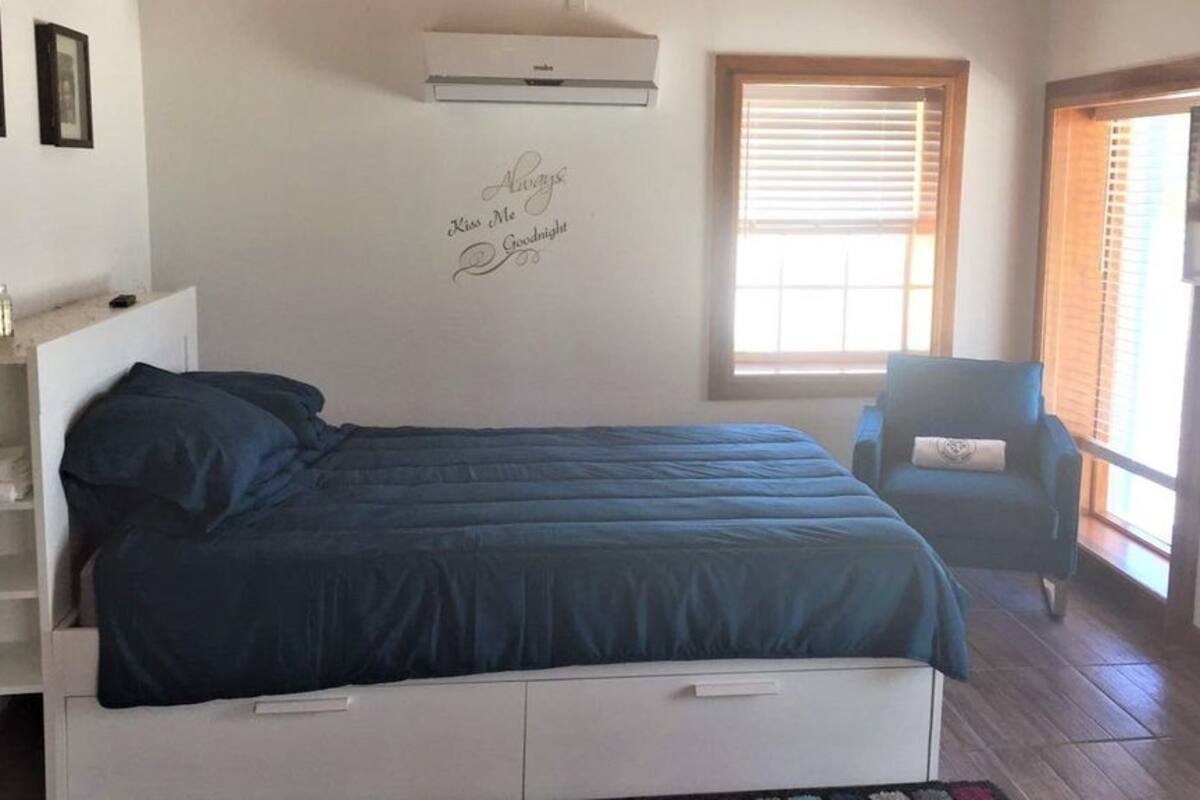 Ein Schlafzimmer mit einem Bett, einem Sessel, einem Fernseher und einem Fenster mit Jalousien.